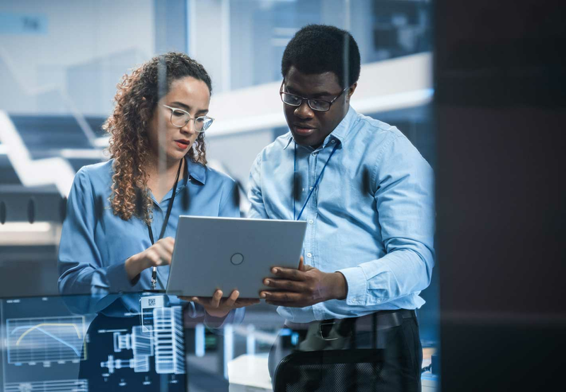 Two engineers, a man and a woman, discuss a project while looking at a laptop.